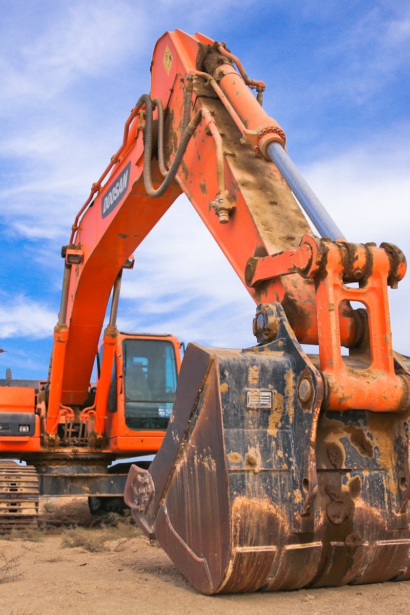 A large orange excavator working on a construction site under a blue sky.